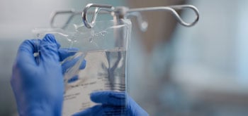 A person wearing blue gloves holds an IV bag filled with clear liquid.